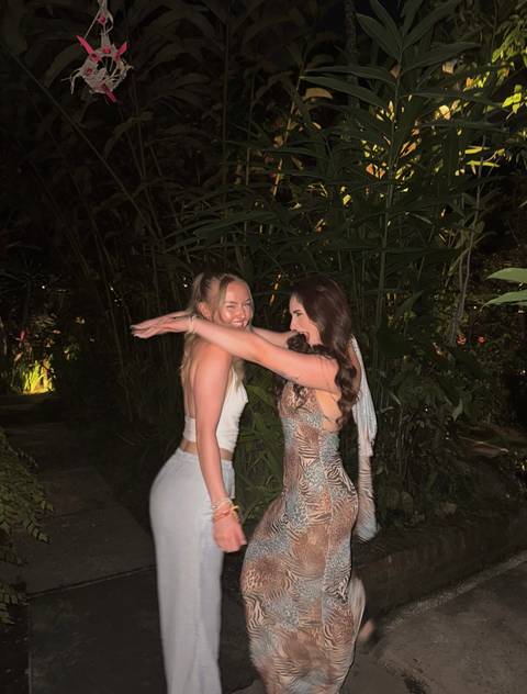       Two friends laughing and posing in a garden setting at night.
  