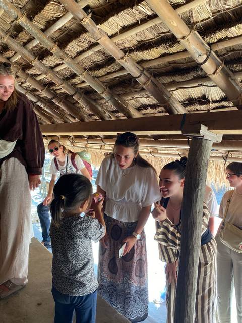 Friends interacting with a local child under a thatched roof.
