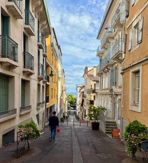       Narrow street with colorful buildings leading to distant water view.
  