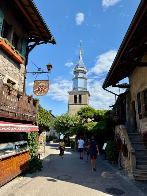      A street view with a tower and restaurant sign in Gruyeres.
  