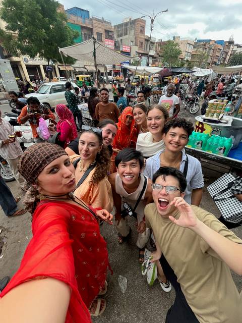       Group of people taking a selfie in a market with locals.
  