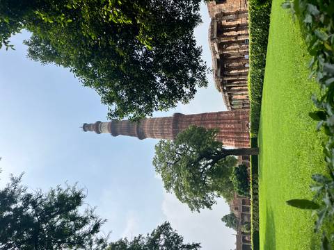       Qutb Minar with green lawns and trees.
  