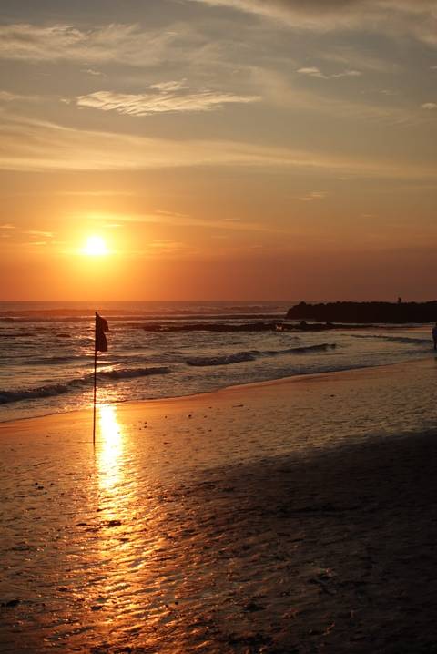 Sunset at a beach with waves and a flag.
