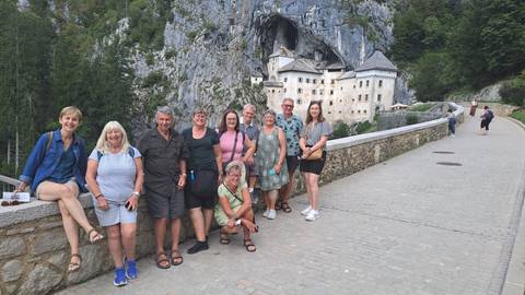 Group of people standing in front of a historic castle built into a cliff.