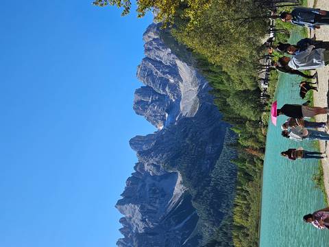 Mountains and a lake with people in the foreground, including a pink umbrella.