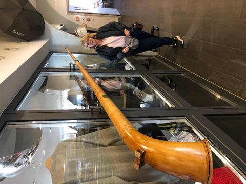 Woman standing next to a long wooden horn in a museum.