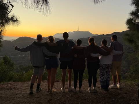 Group of people with arms around each other looking at the Hollywood sign at sunset.