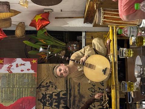       Musician sitting and playing a traditional instrument in a decorated room.
  