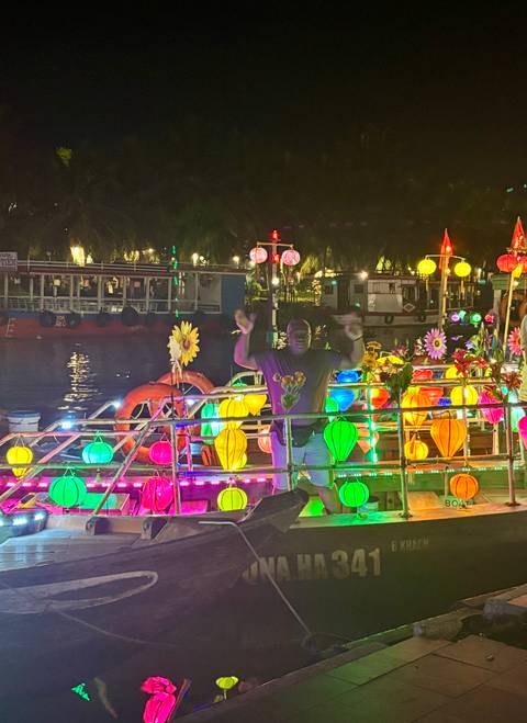       Person surrounded by brightly lit lanterns on a decorated boat at night.
  