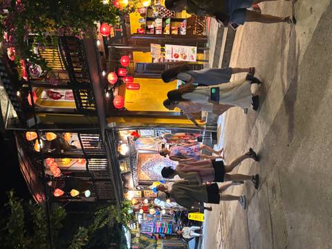       Group of people walking through a street lined with shops and lanterns.
  