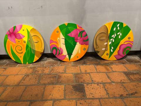       Three colorful round paintings on a brick floor, depicting faces and floral motifs.
  
