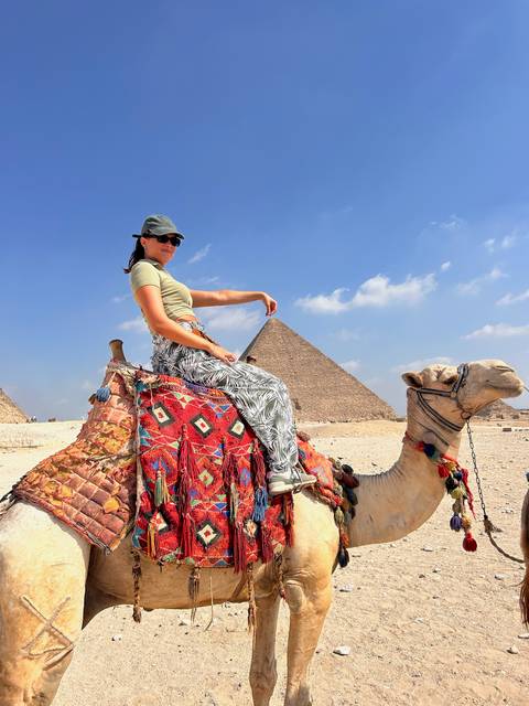 Person riding a camel near the Egyptian pyramids.