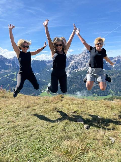       Three people jumping with a mountain range in the background.
  