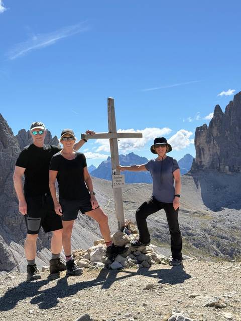       Three people posing with a cross on a mountain.
  