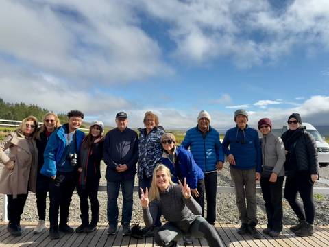       A group of tourists posing outdoors with mountains in the background.
  