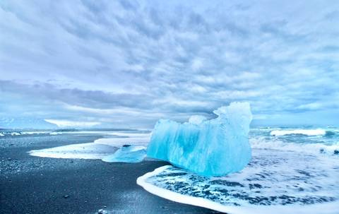       Large ice formation washed ashore on a black sand beach.
  