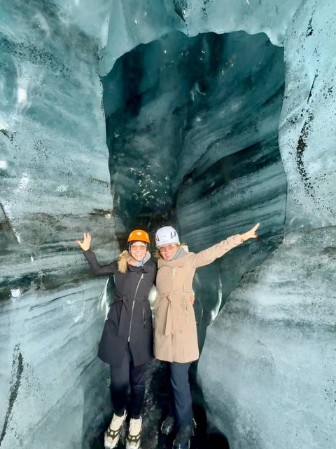 Two people smiling and posing inside a glacier cave.