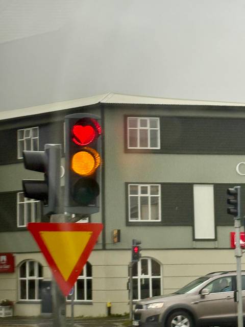 Traffic light with heart-shaped red light against a building backdrop.
