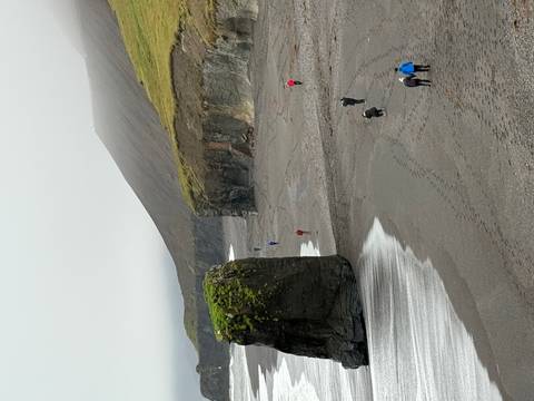       People walking along a rocky coastline under cloudy skies.
  
