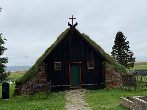       A turf-roofed church surrounded by a grassy field.
  