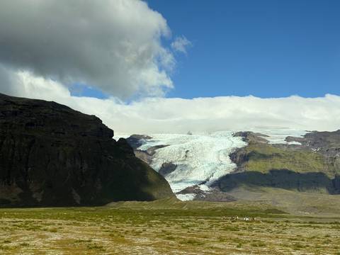 Glacier with surrounding green mountains under a clear sky.