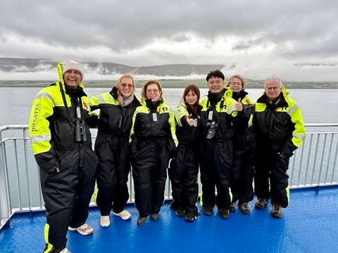       A group of people in winter attire posing on a boat with mountains in the background.
  