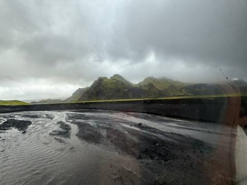       Black sand beach with rocky mountains under overcast skies.
  