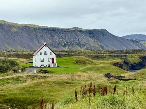      White house on a grassy field with cliffs in the background.
  