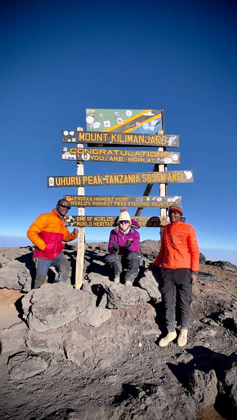 Three hikers posing at Uhuru Peak summit sign.