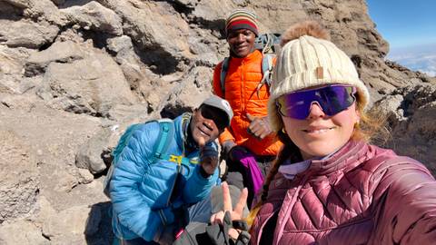 Three hikers with climbing gear on a rocky path.
