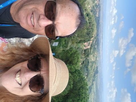       A man and woman taking a selfie with a panoramic view of the countryside.
  