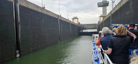       People on a boat passing through a lock with high concrete walls.
  