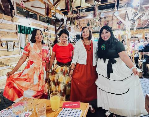 Women in colorful dresses standing and smiling indoors.
