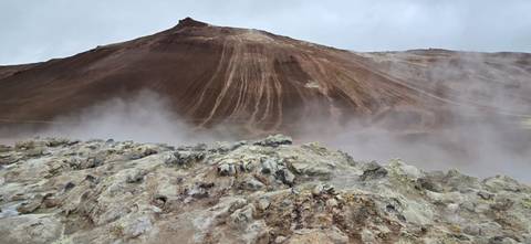 Steaming geothermal landscape with barren rocky hills.
