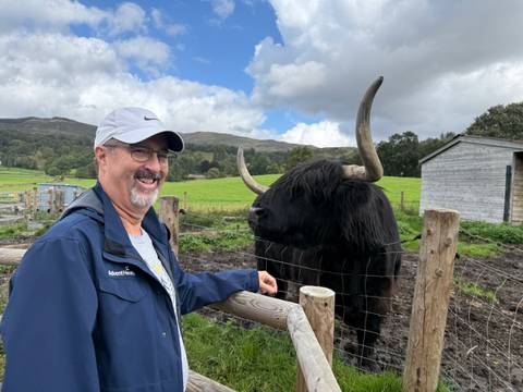 Man standing by a Highland cow at a fence.