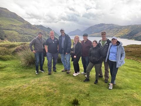 A group of people posing in front of a scenic view with hills and a body of water.