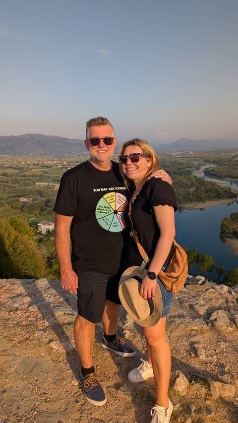       Couple posing for a photo with a scenic river view in the background.
  