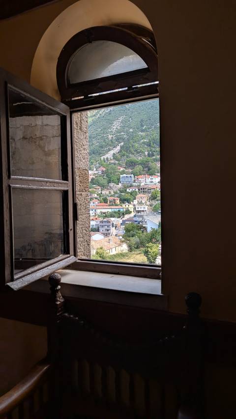       View of a village through a stone window with traditional houses and rolling hills.
  