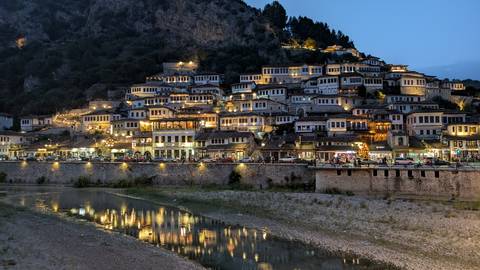       Night view of Berat, showcasing illuminated historic houses along the river.
  