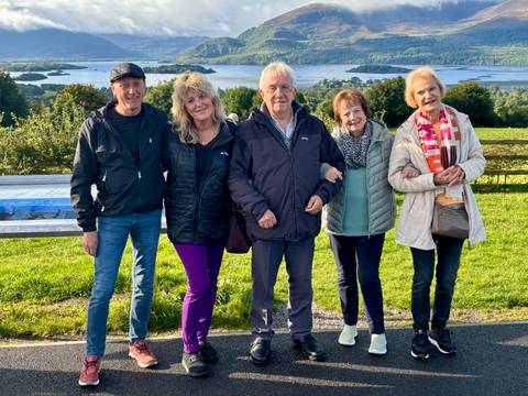 A group of people posing in a park with a lake and hills in the background.