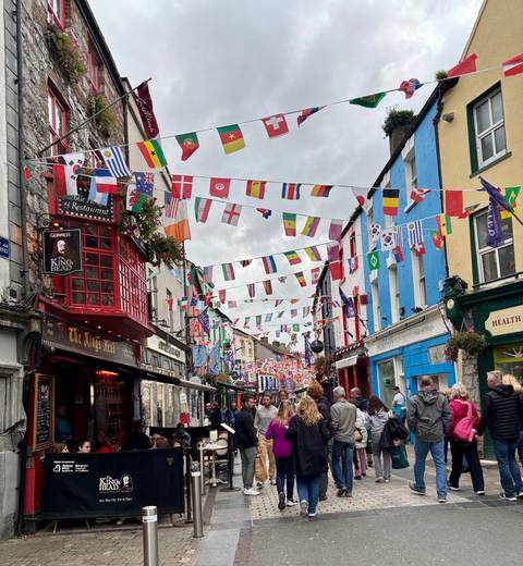 Street with colorful flags and shops, bustling with people.