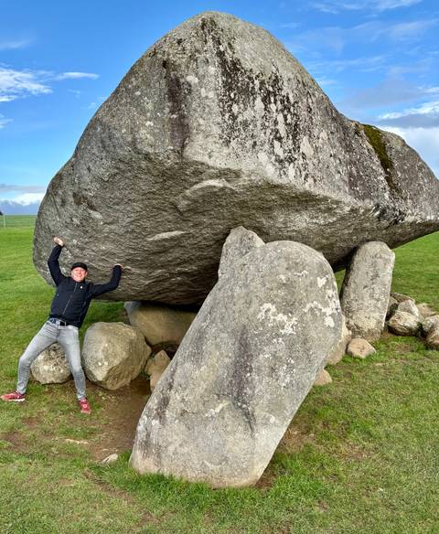 Person posing under a large balancing rock.