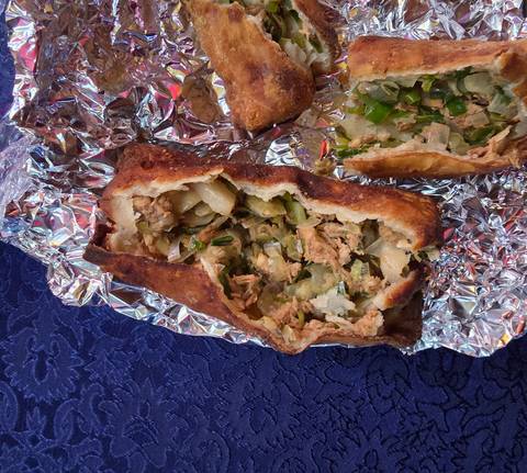 Close-up of a cut open pastry with meat filling on foil.