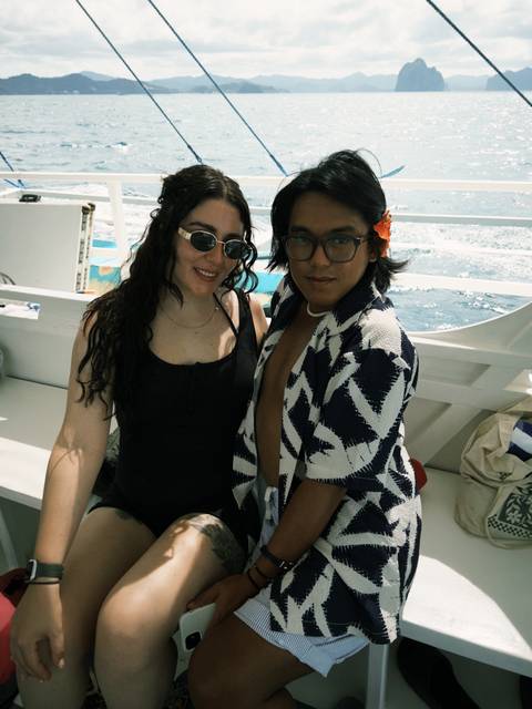 Two people wearing sunglasses and colorful clothing on a boat with ocean waves.