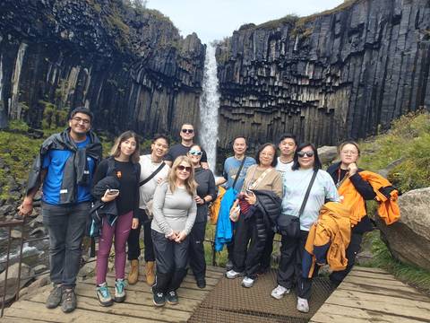 Group of people posing in front of a waterfall with basalt columns.