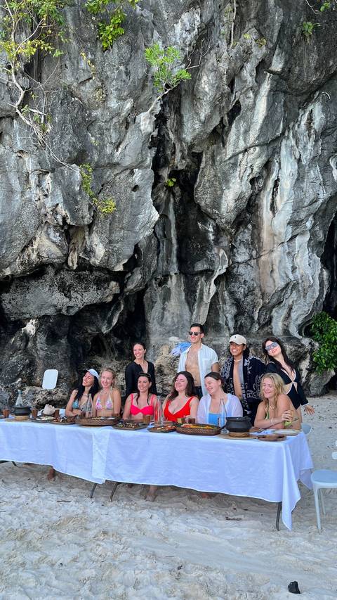 Group of people posing in front of a rocky cliff on a beach.