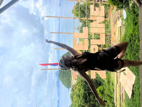 Woman in zip-lining equipment posing with an ocean view backdrop.