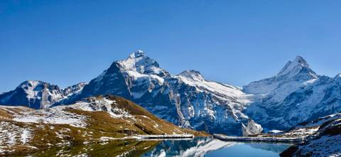 Snow-capped mountains reflecting in a clear lake under a blue sky.