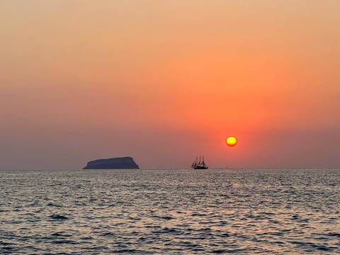 A majestic sunset over the sea with a distant sailboat.
