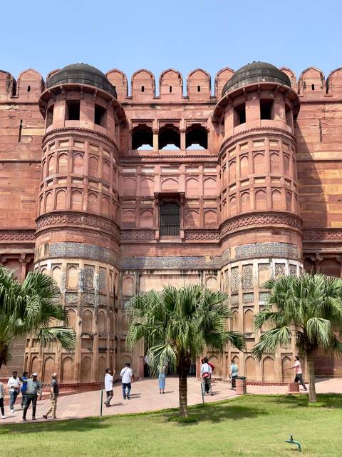 Ornate red sandstone fort with lush green bushes at the base.